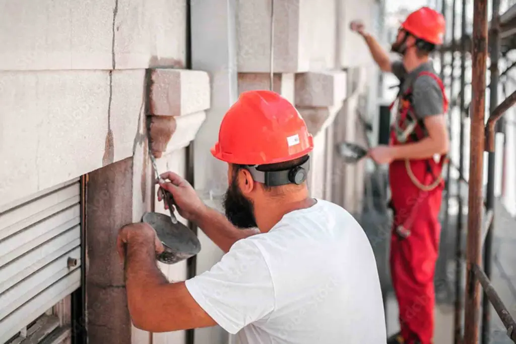 dos trabajadores están reparando grietas de la fachada